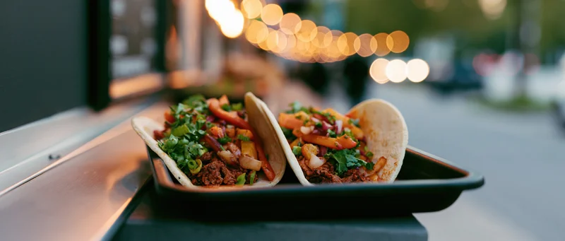 Two loaded street tacos in a black tray on a food truck at night