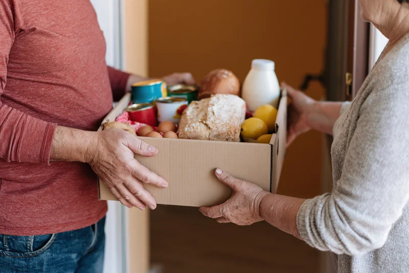 Two people passing a cardboard box of groceries at a doorway