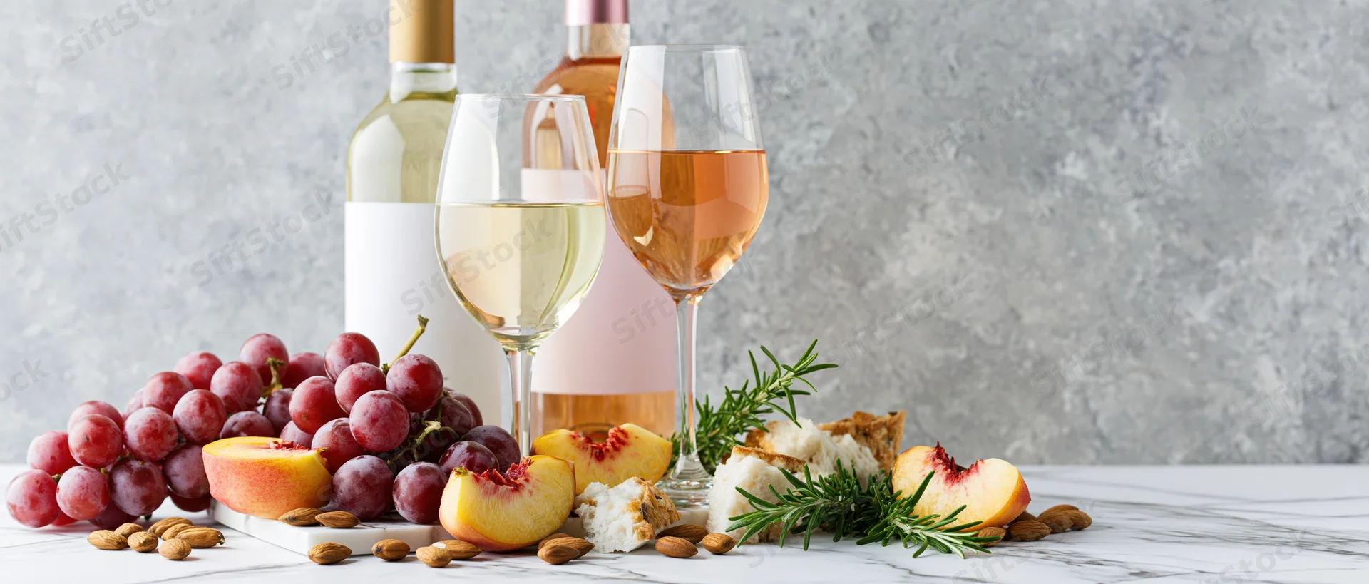 Wine bottles and glasses with grapes, peaches, cheese, and almonds arranged on a marble table