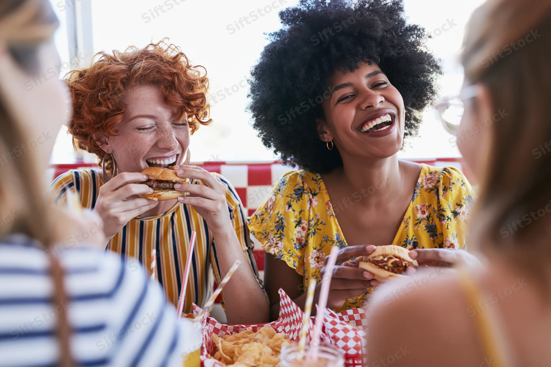 Two women laughing and eating burgers at a diner booth