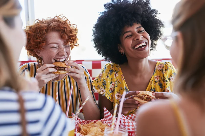 Two women laughing and eating burgers at a diner booth