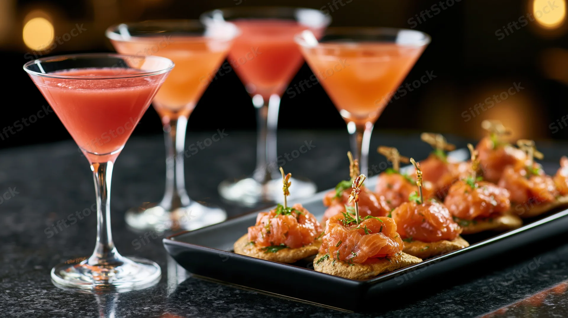Four pink cocktails and salmon canapes on a dark table at an upscale party