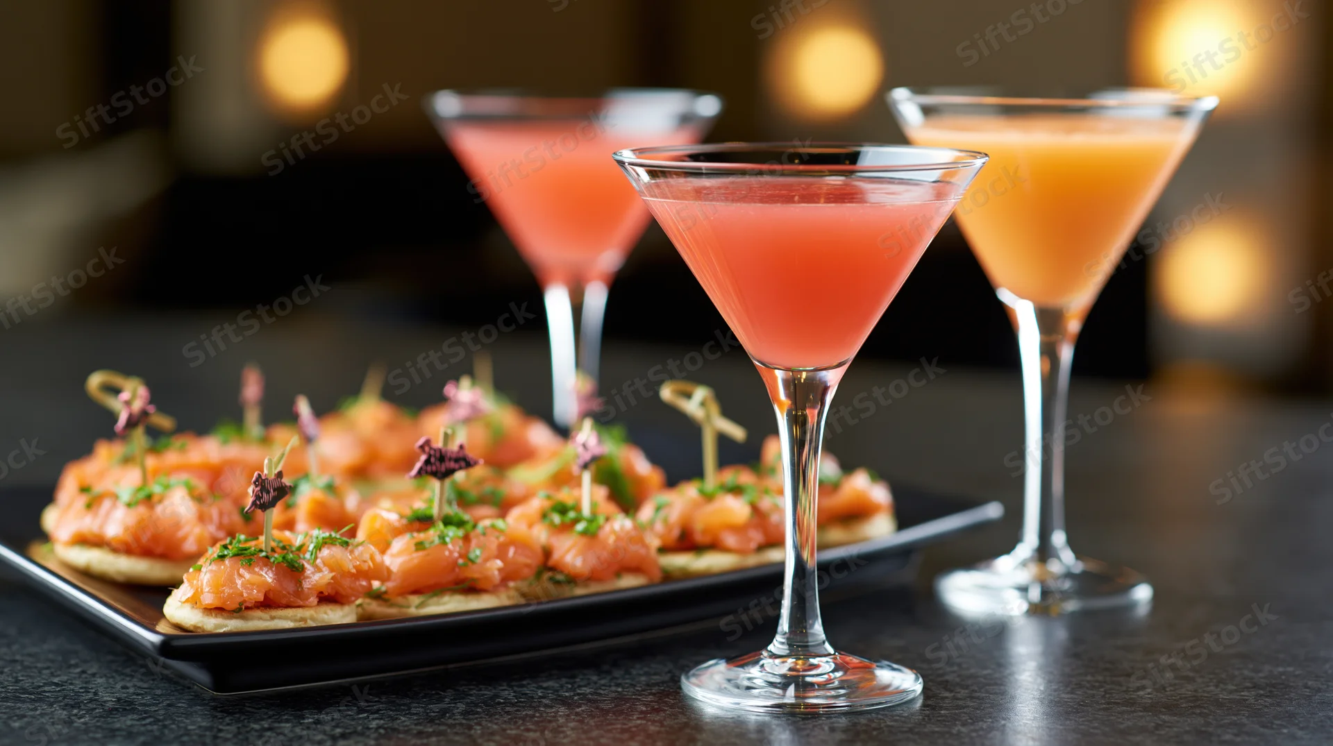 Three cocktails and smoked salmon canapes on a dark polished table at an upscale party