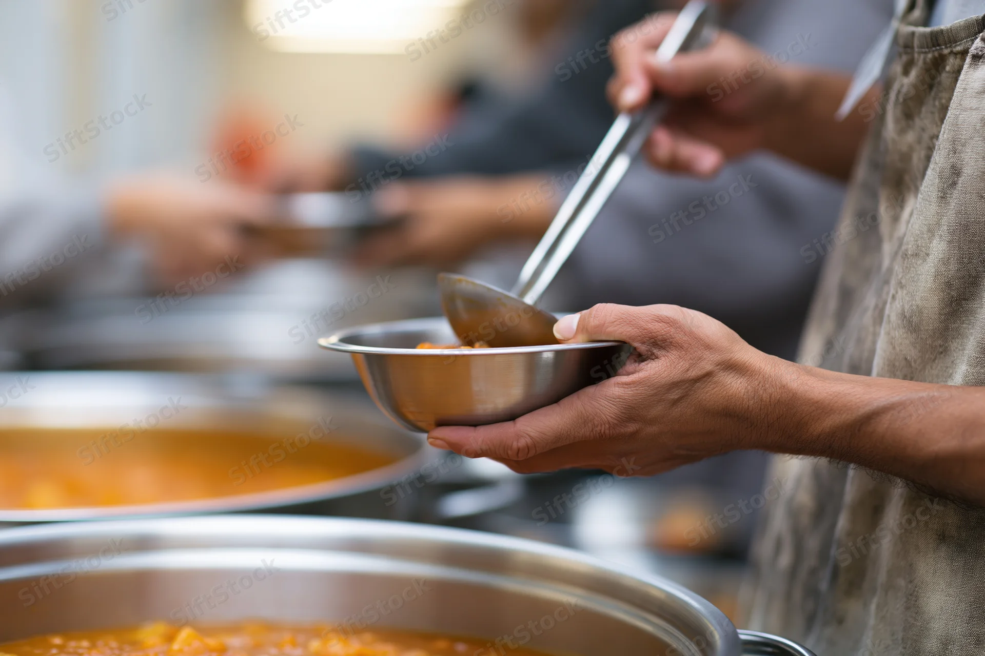 Volunteer ladling hot soup into a metal bowl in a community kitchen