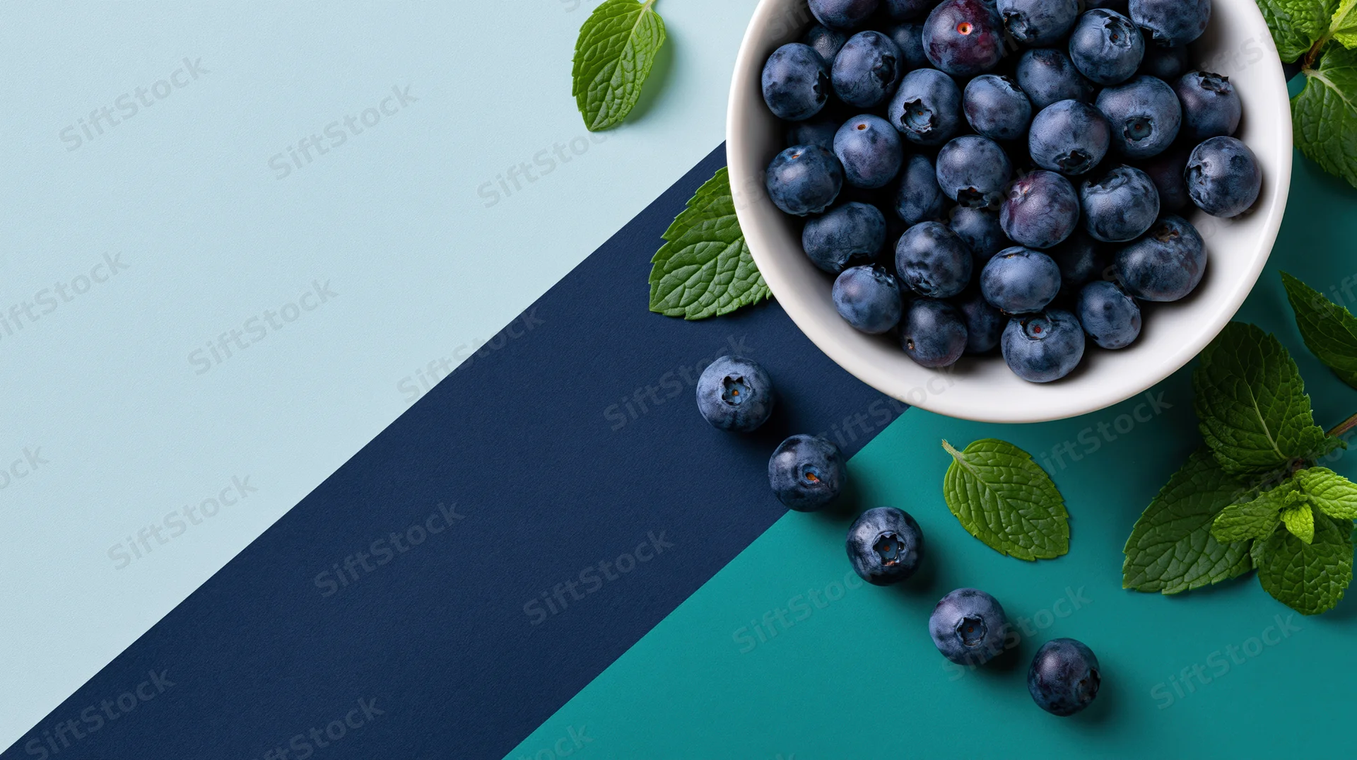White ceramic bowl filled with fresh blueberries and mint leaves on a blue and teal background