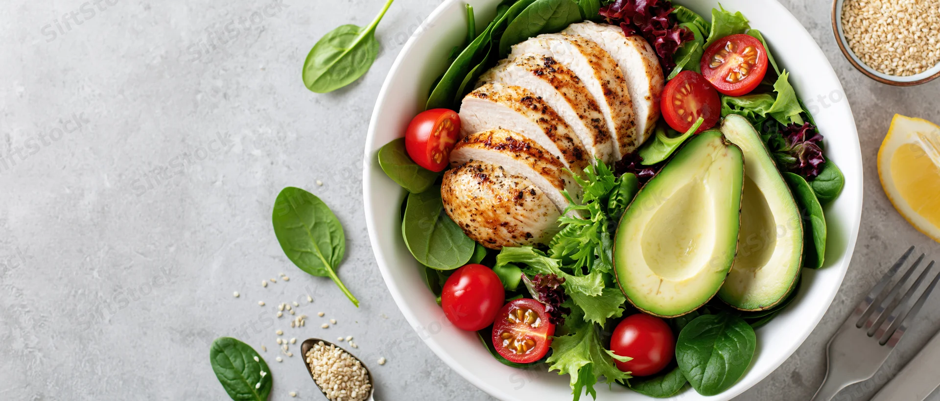 Grilled chicken and avocado salad in a white bowl with spinach and cherry tomatoes on a light surface