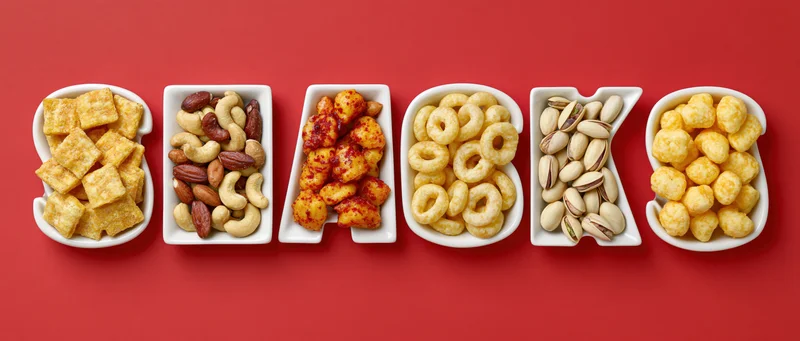 Ceramic bowls shaped as letters spelling snacks filled with various snacks on red background