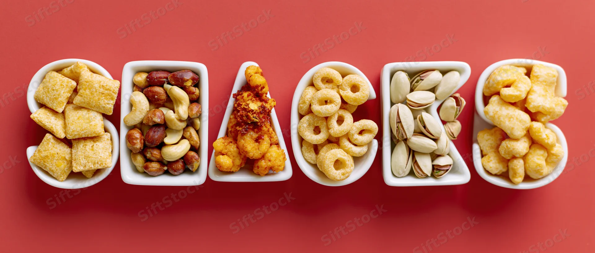 Ceramic dishes shaped like letters spelling snacks filled with various foods on red background