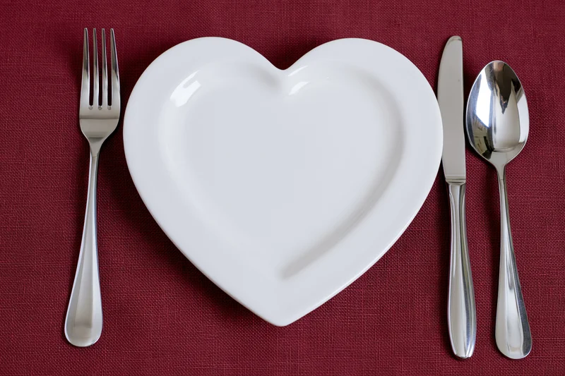 Heart-shaped white ceramic plate with silverware arranged on red linen tablecloth