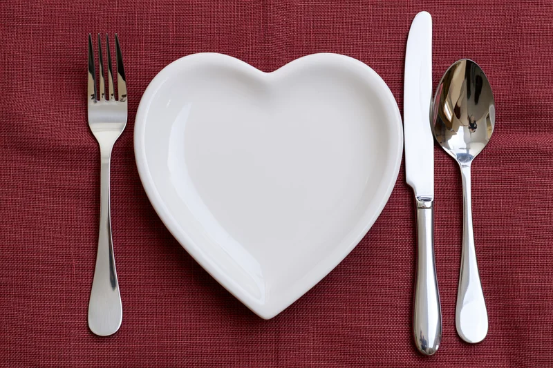 Heart-shaped white ceramic plate with silverware arranged on red linen tablecloth