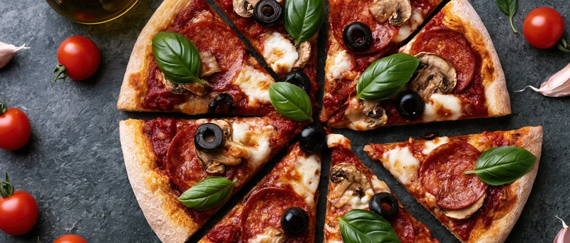 Sliced pepperoni and mushroom pizza with basil and olives on dark slate surface