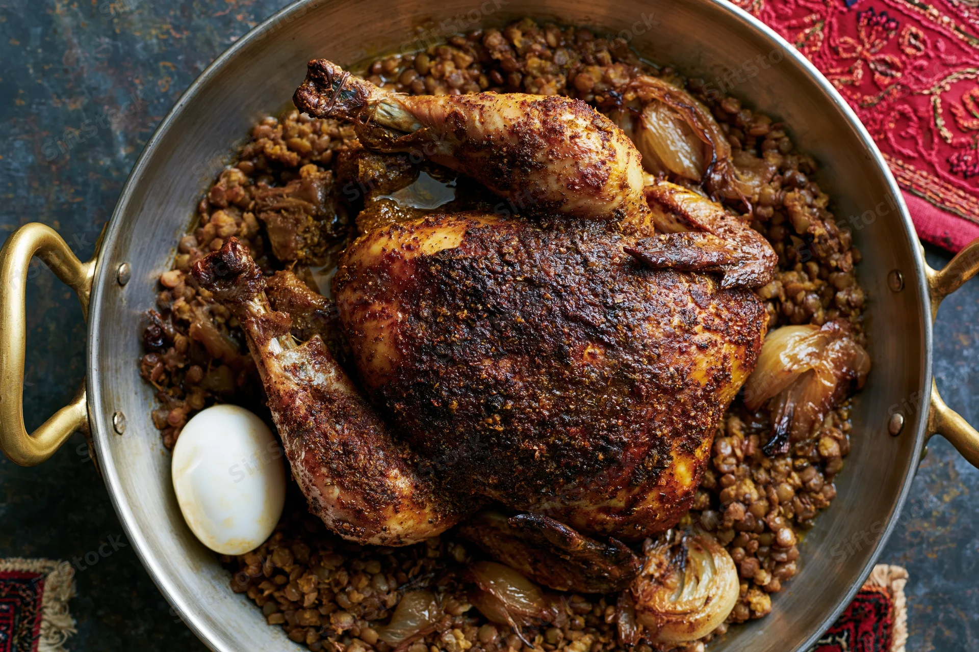 Whole roasted spiced chicken in a brass-handled pan with lentils and onions