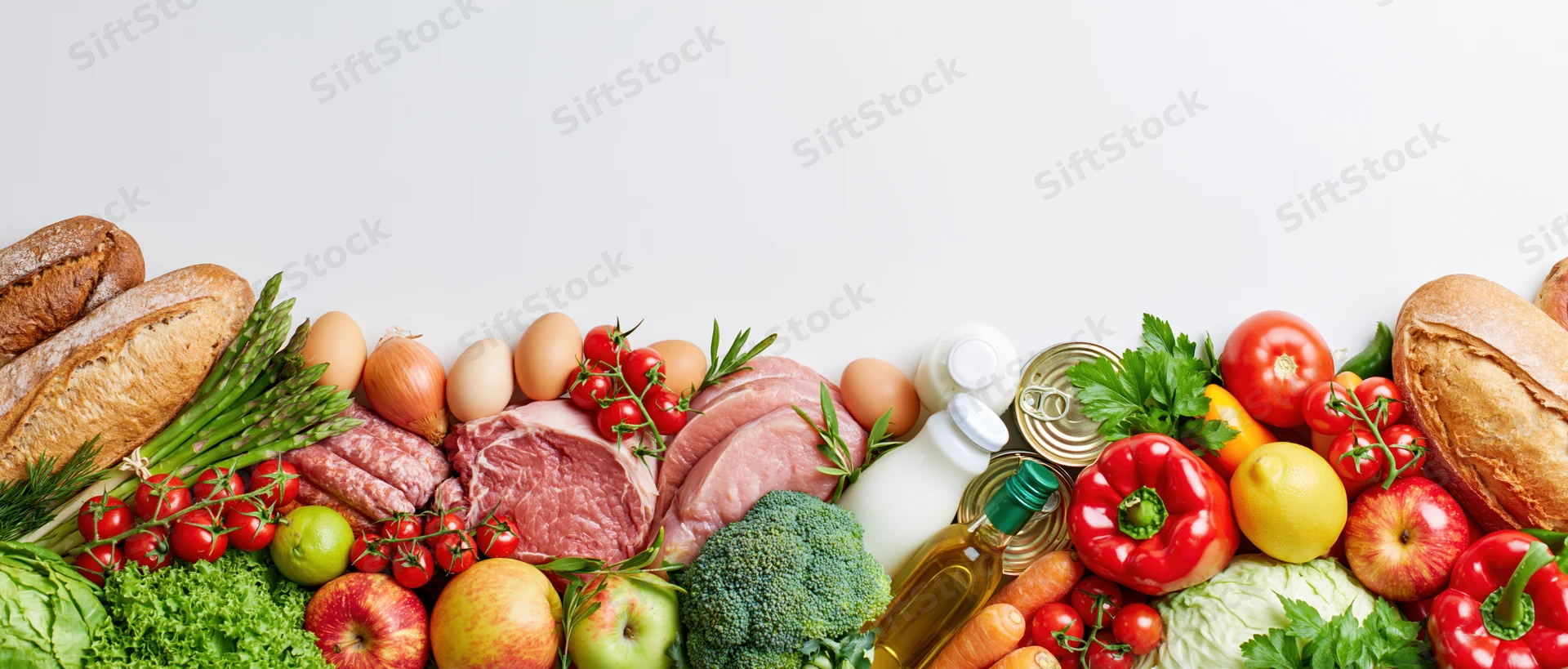 Wide flat-lay arrangement of mixed groceries piled along bottom edge against white background