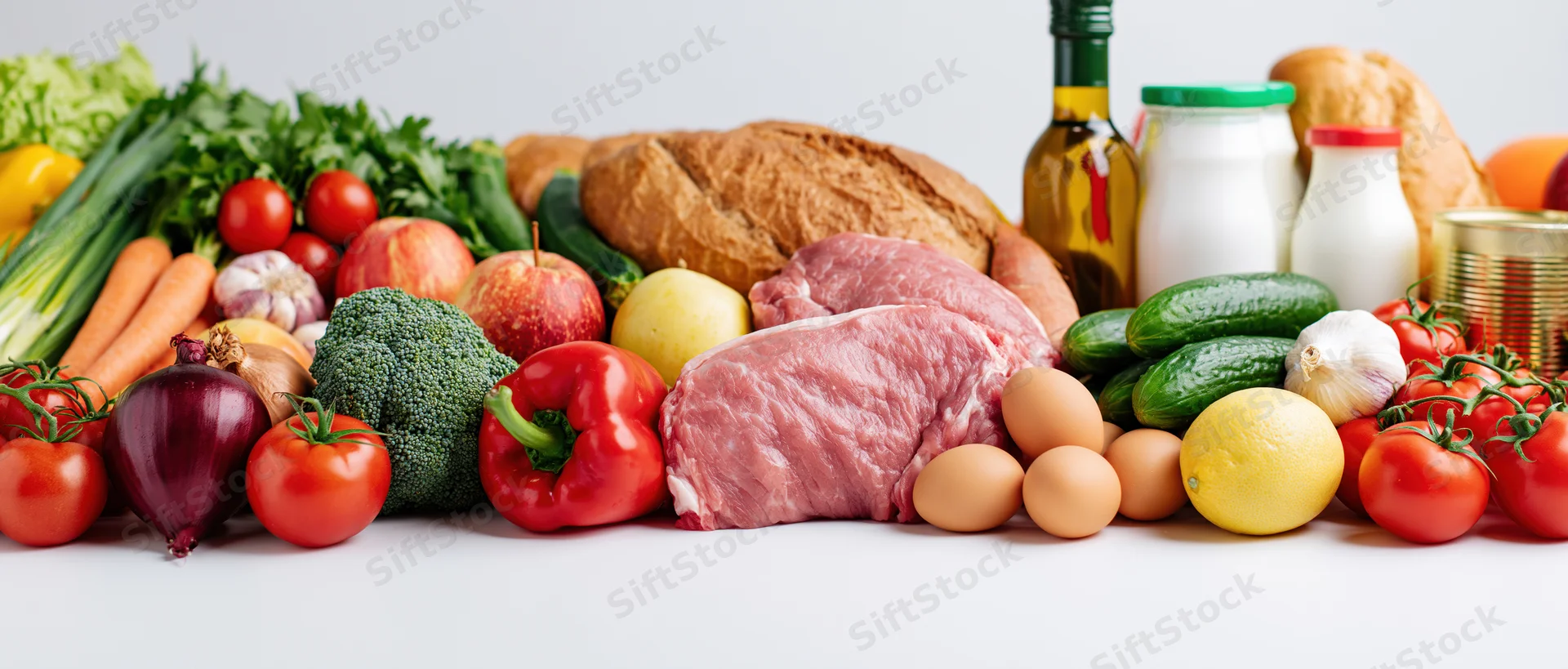 Wide flat-lay arrangement of mixed groceries piled on white surface