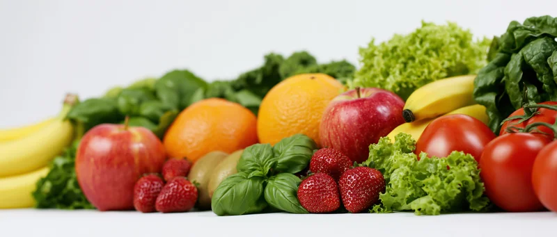 Wide horizontal arrangement of fresh fruits and vegetables on white background