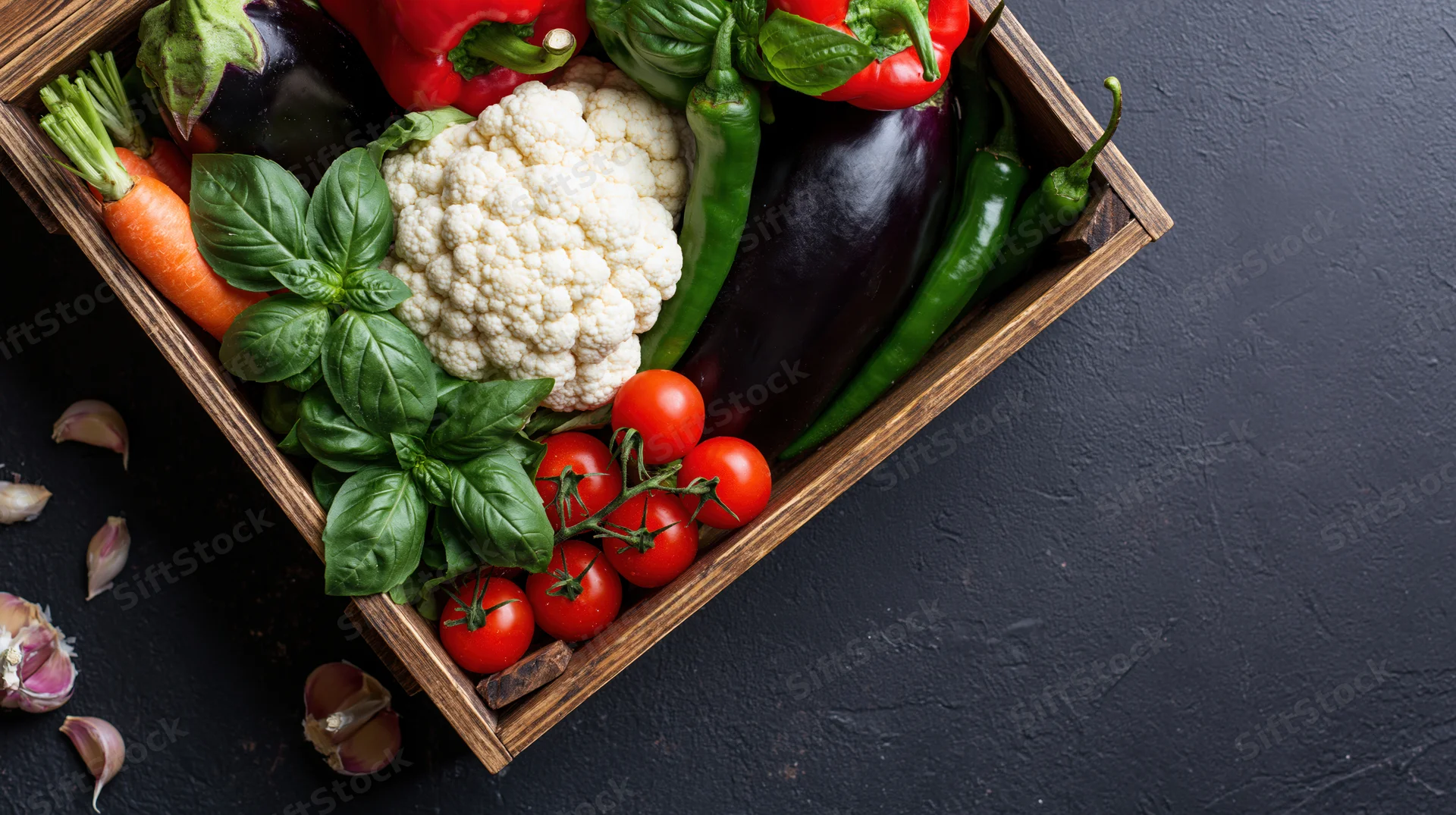 Fresh vegetables arranged in a wooden crate on a dark surface