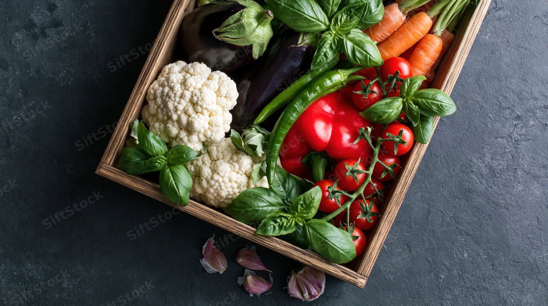 Wooden crate filled with fresh vegetables on dark surface