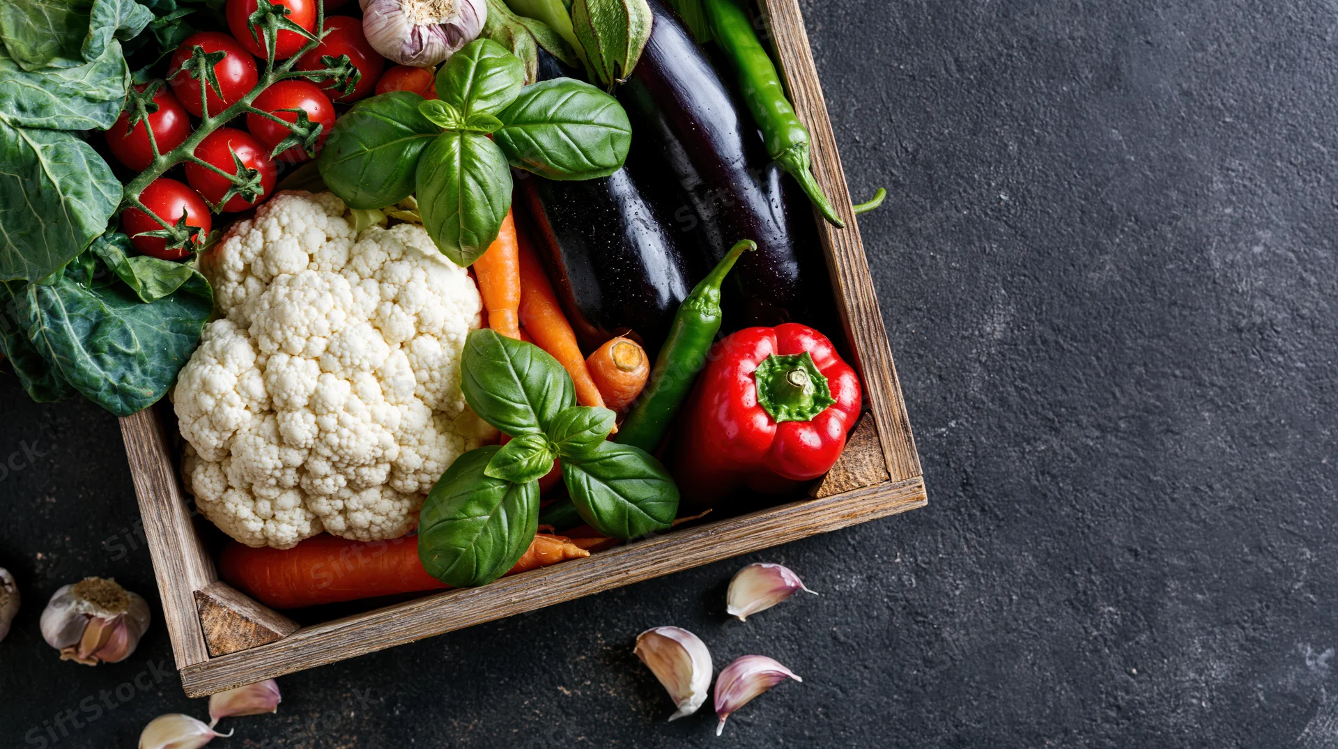 Fresh vegetables arranged in a wooden crate on a dark stone surface