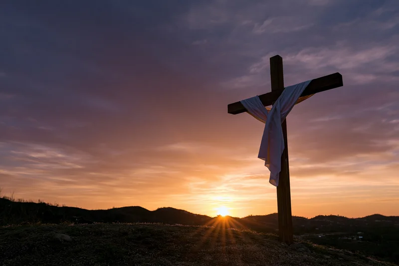 Wooden cross with white cloth draped over it standing on a hill at sunset