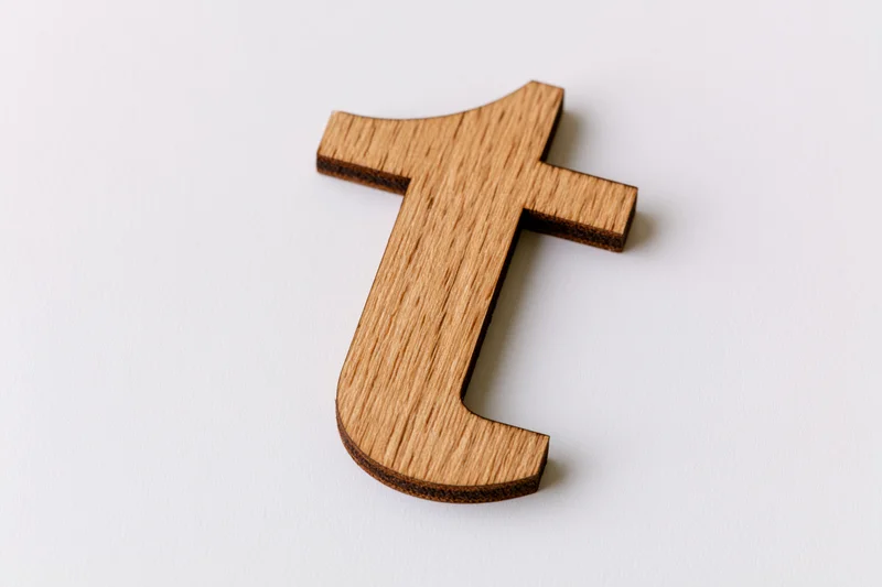 Wooden lowercase letter t cutout lying flat on a white surface