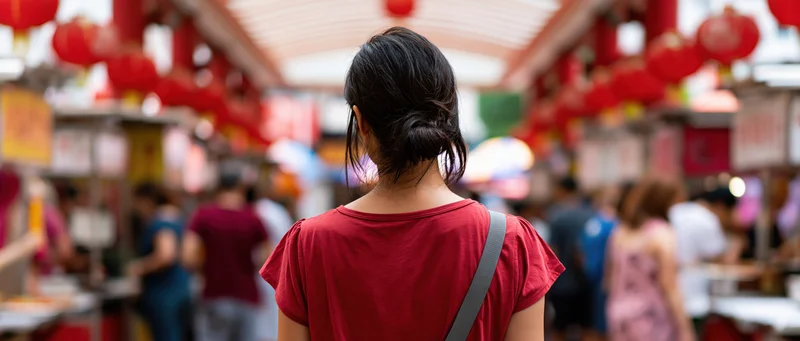 Asian woman walking through a busy outdoor market with red lanterns overhead
