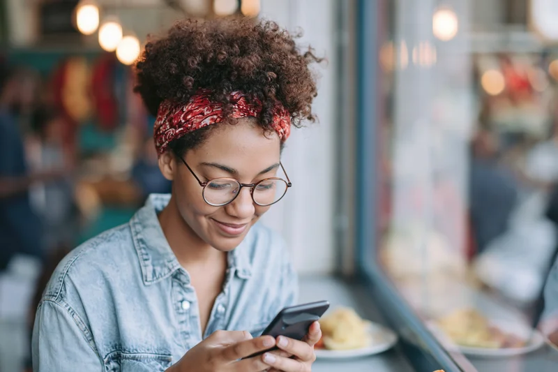 Young black woman smiling while using smartphone in a cafe interior