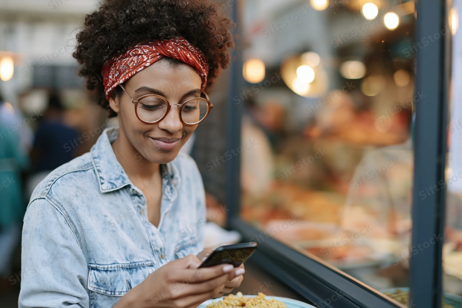 Young black woman smiling while texting on smartphone outdoors near food market display