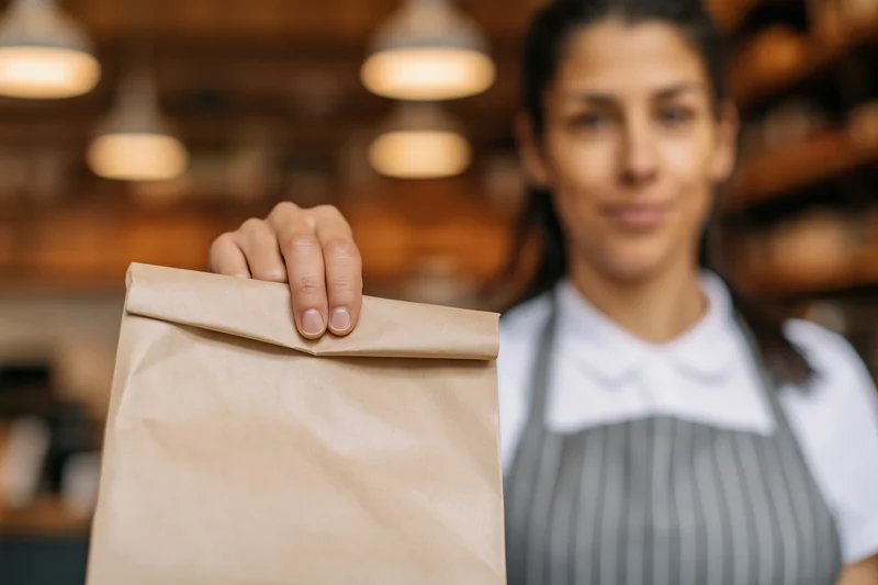 Woman holding a kraft paper takeout bag in a cafe