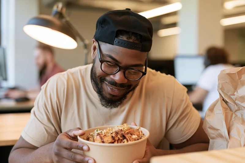 Man eating takeout lunch at office desk smiling