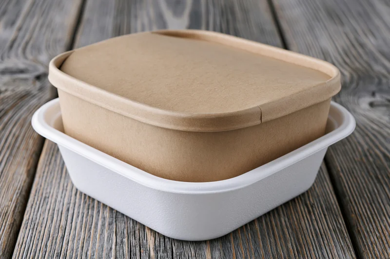 Kraft cardboard sleeve over white foam food container on wooden surface