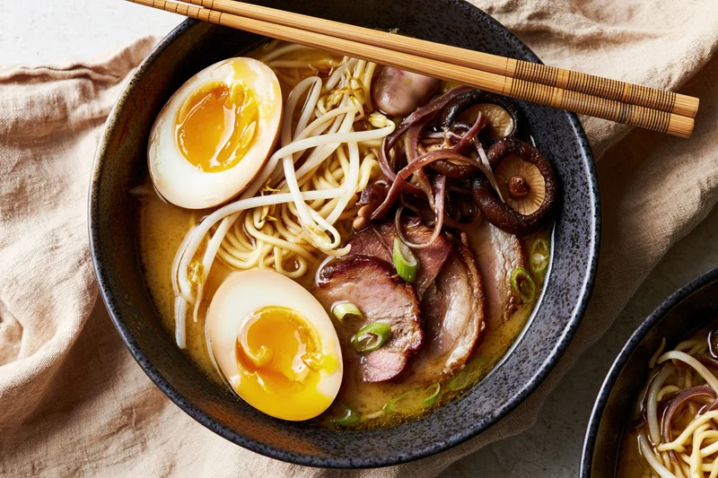 Bowl of ramen with soft-boiled eggs, pork, mushrooms and bean sprouts on a linen cloth