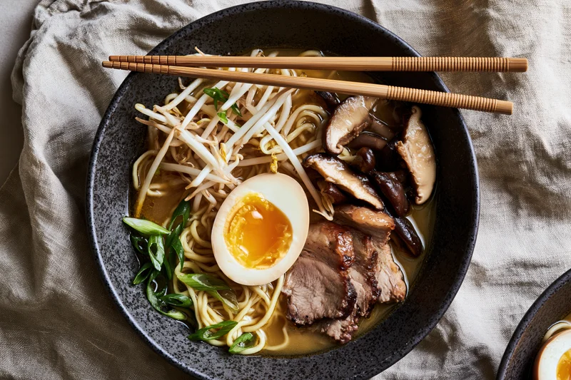 Bowl of japanese ramen with soft-boiled egg, mushrooms, pork, bean sprouts and green onions, overhead view on linen cloth
