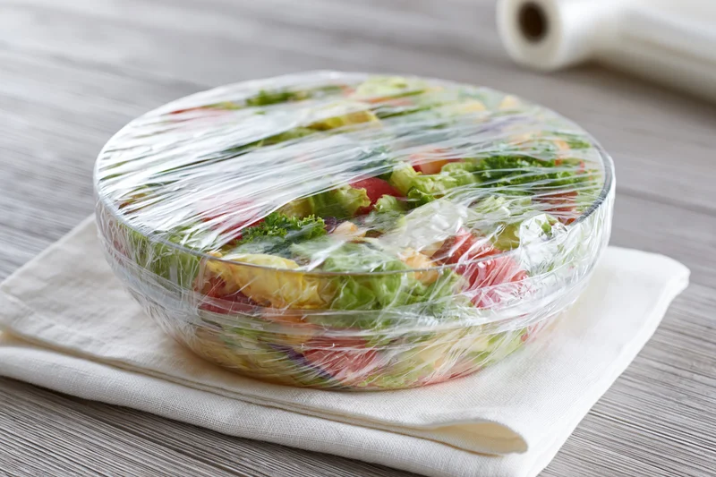 Bowl of fresh vegetable salad covered with plastic wrap on a kitchen countertop