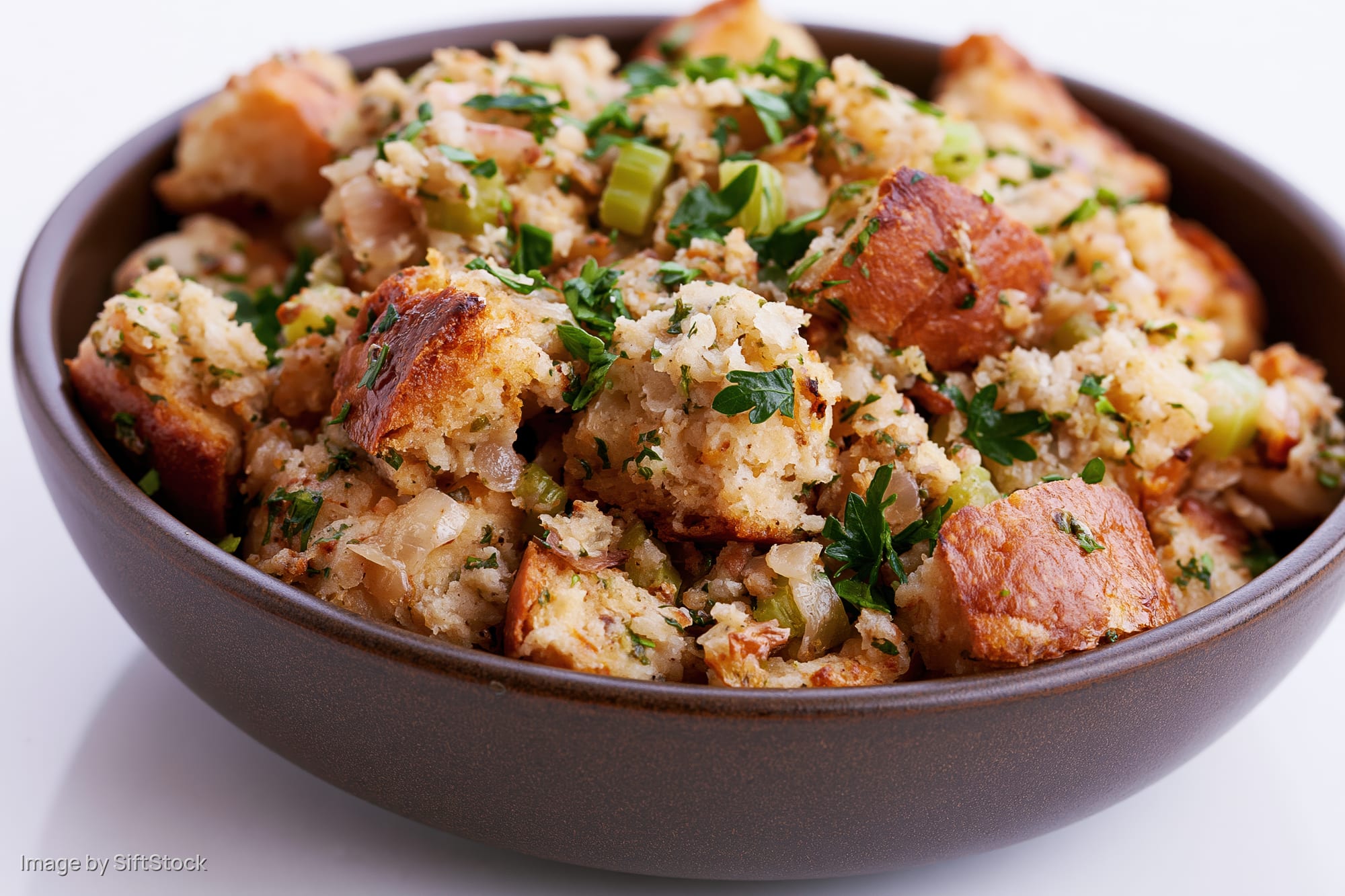 Bowl of rustic bread stuffing with toasted cubes and herbs on white background