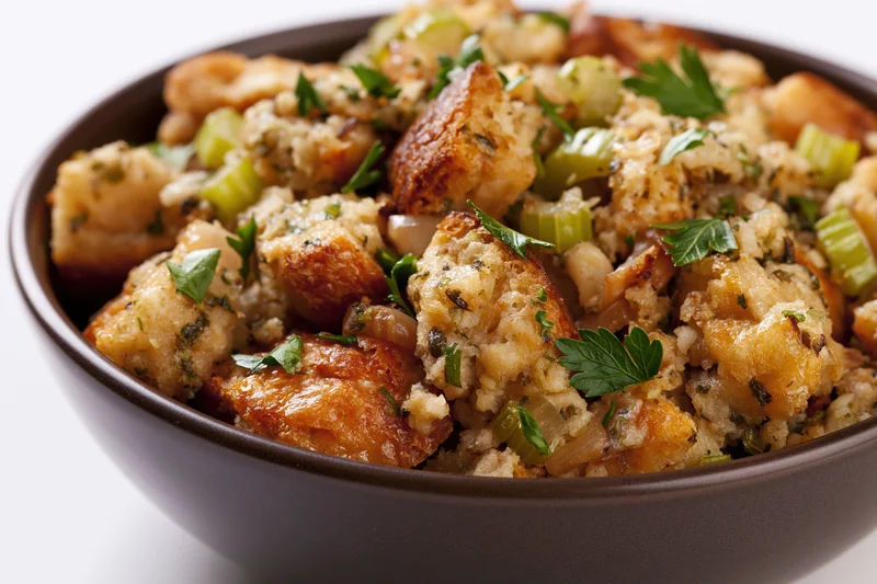 Bowl of rustic bread stuffing with toasted cubes and herbs on white background