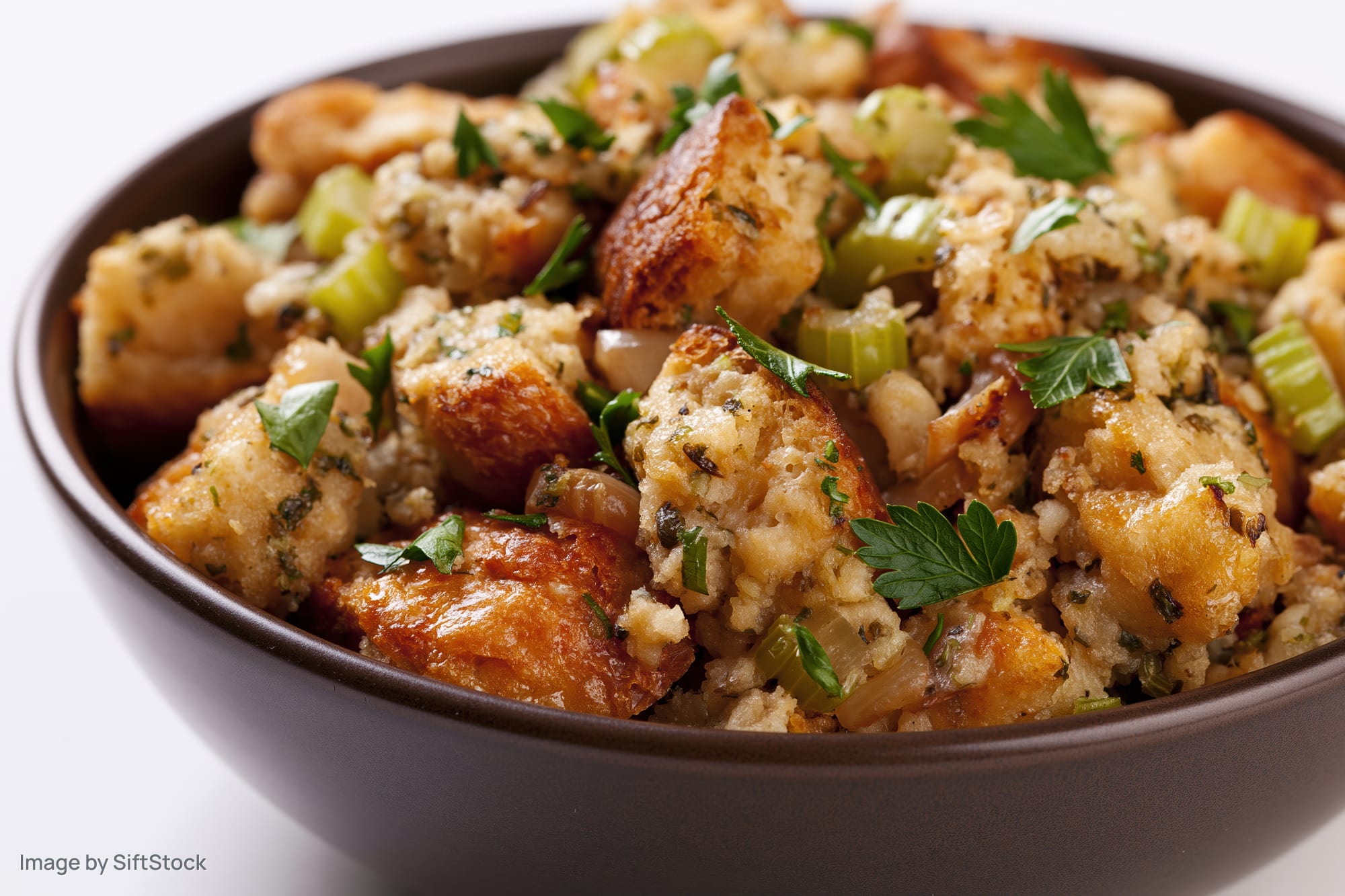 Bowl of rustic bread stuffing with toasted cubes and herbs on white background
