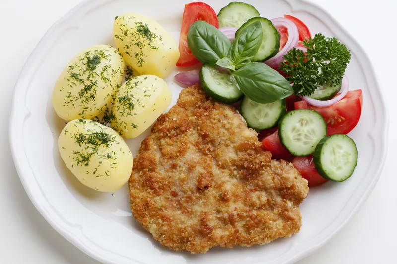 Breaded pork schnitzel with boiled potatoes and vegetable salad on a white ceramic plate