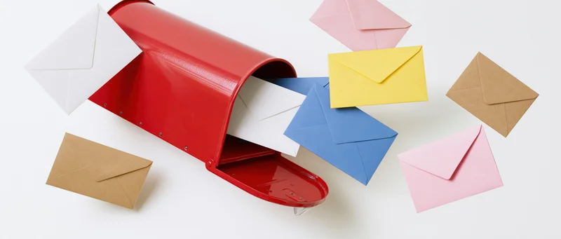 Red metal mailbox open with colorful envelopes scattered around on white background