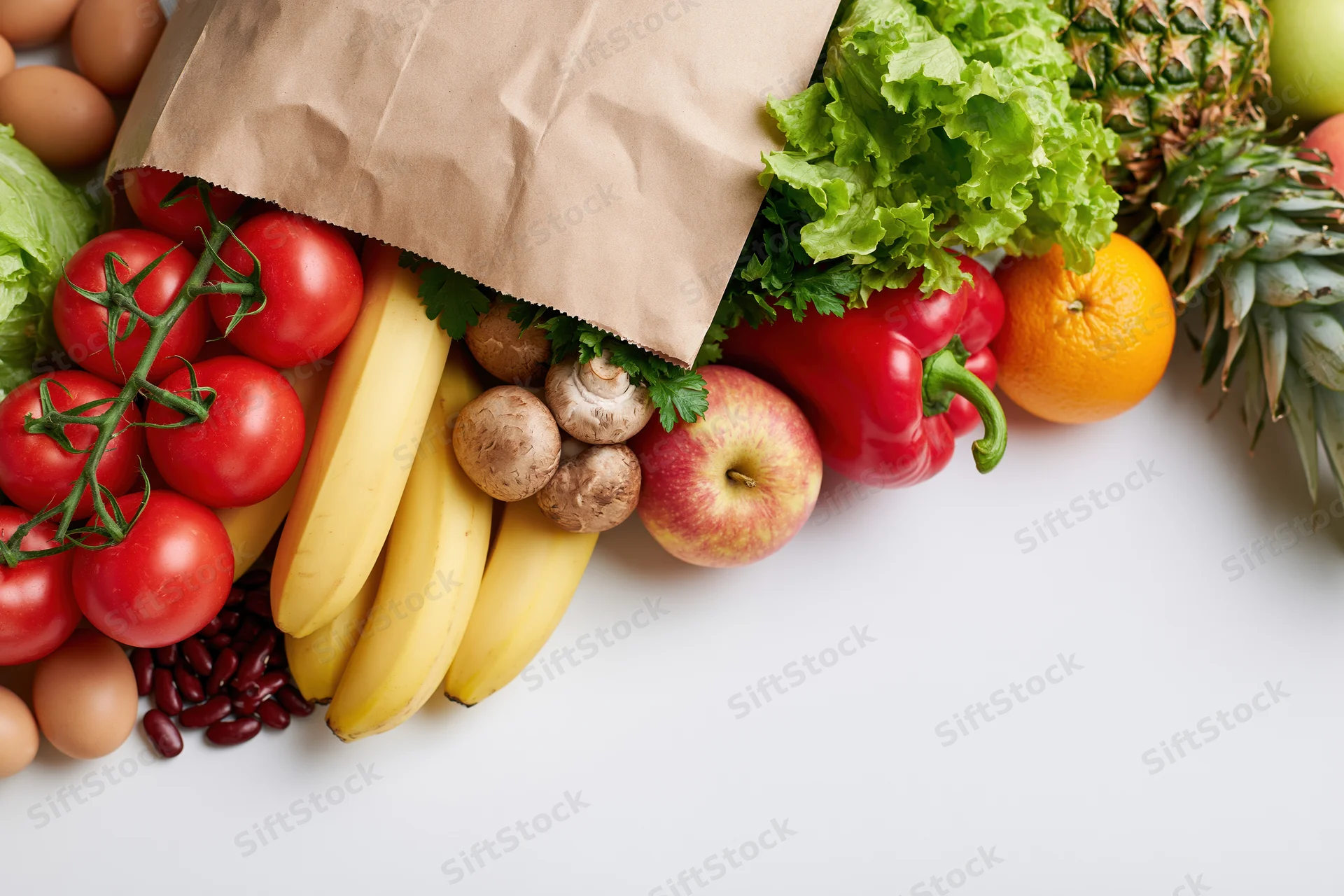 Brown paper grocery bag tipped on its side spilling fresh fruits and vegetables onto white surface