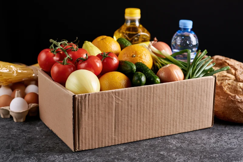 Cardboard box filled with fresh vegetables and fruit on dark surface