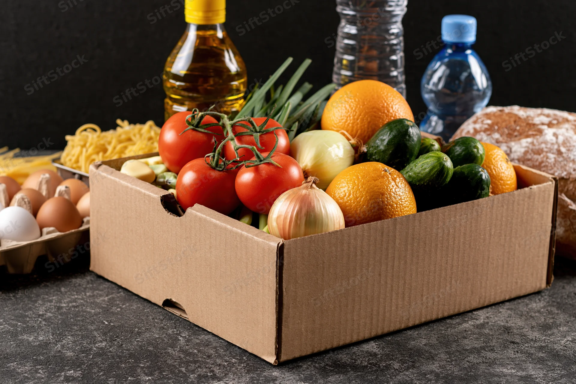 Cardboard box filled with fresh vegetables and fruit on dark surface