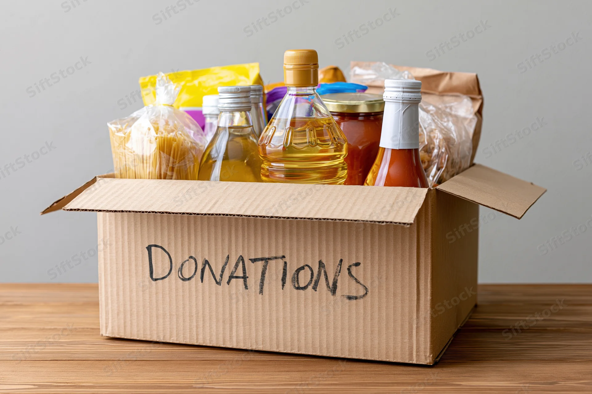 Open cardboard box labeled donations filled with food items on wooden table