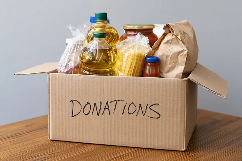 Cardboard box labeled donations filled with nonperishable food items on wooden table