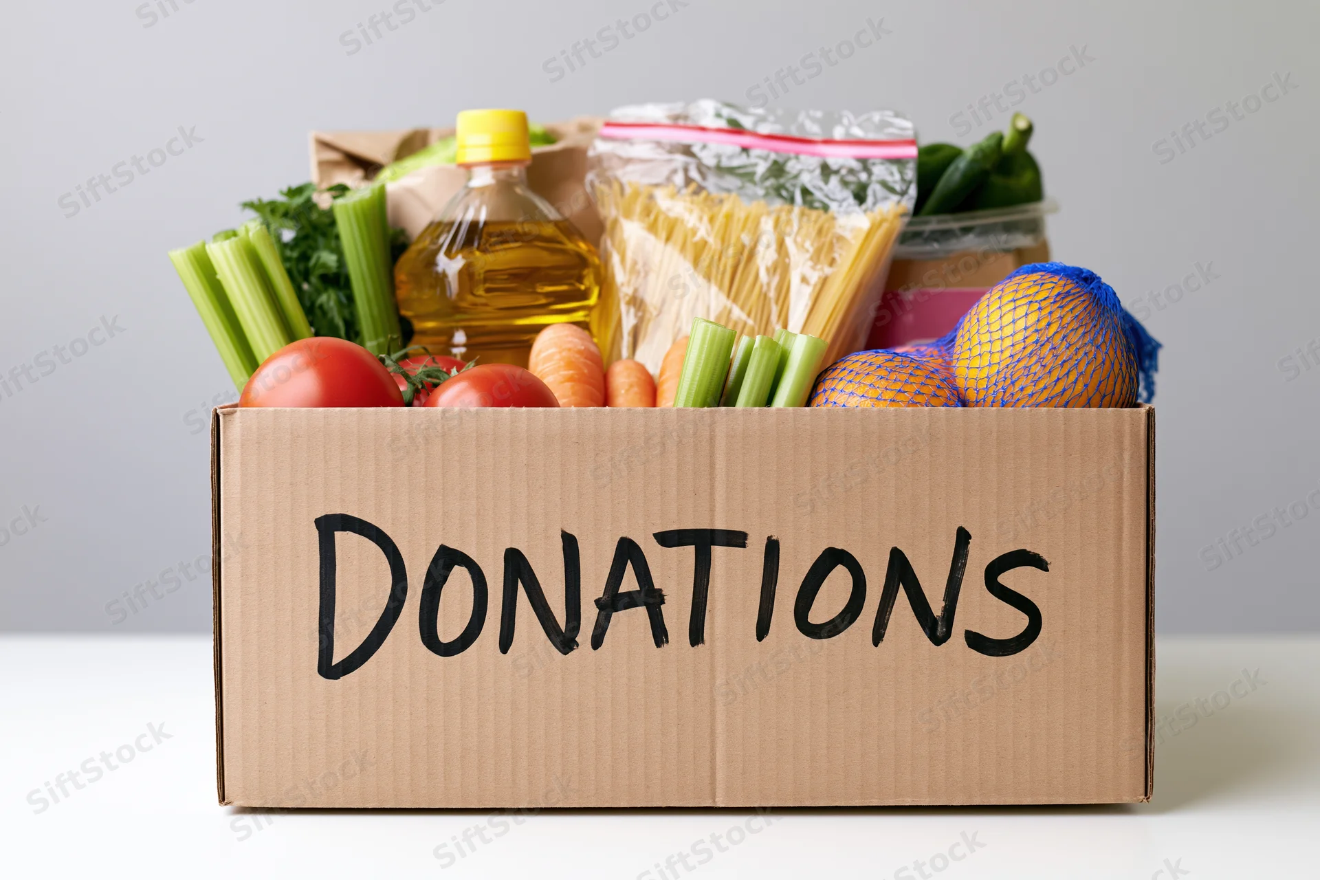 Cardboard box labeled donations filled with groceries and food items on a white surface