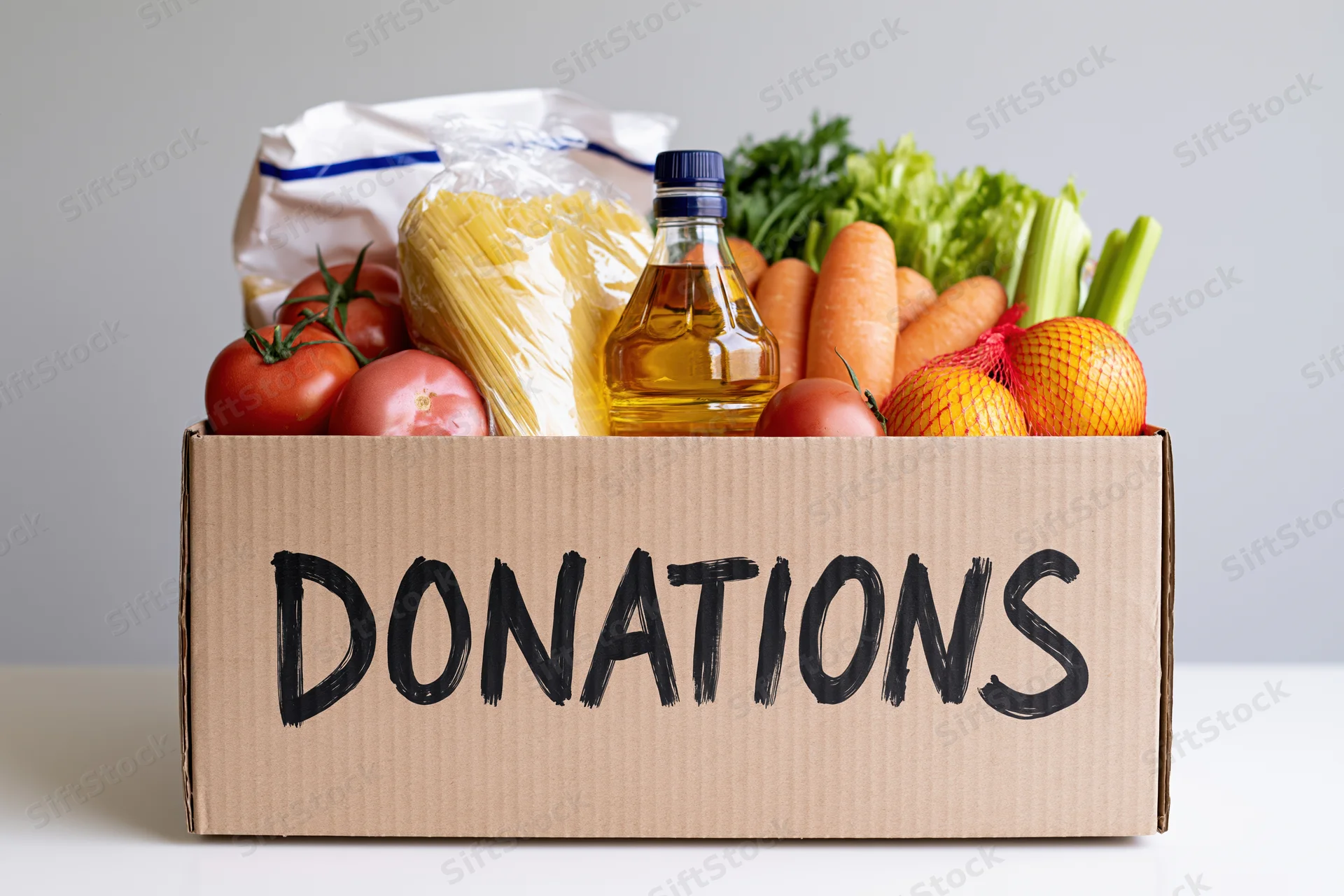 Cardboard box filled with groceries labeled donations on a white surface