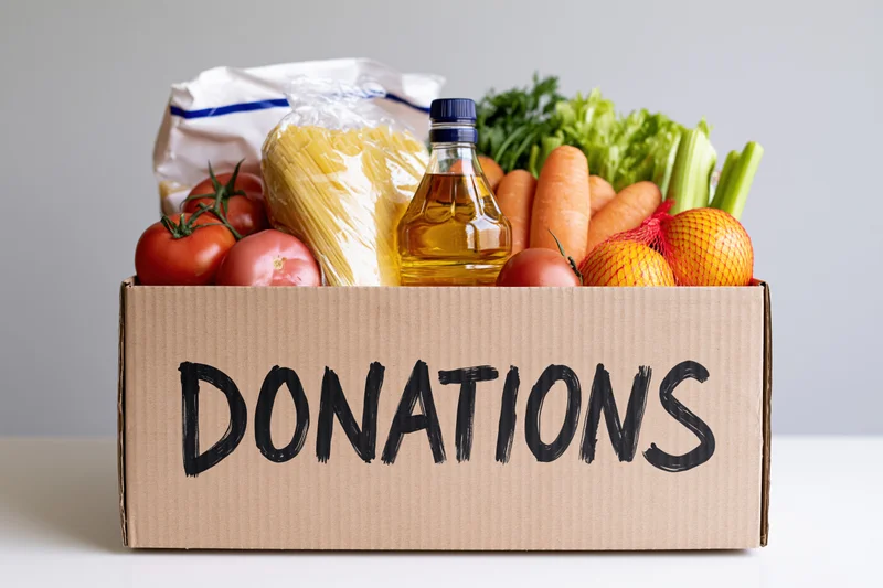 Cardboard box filled with groceries labeled donations on a white surface
