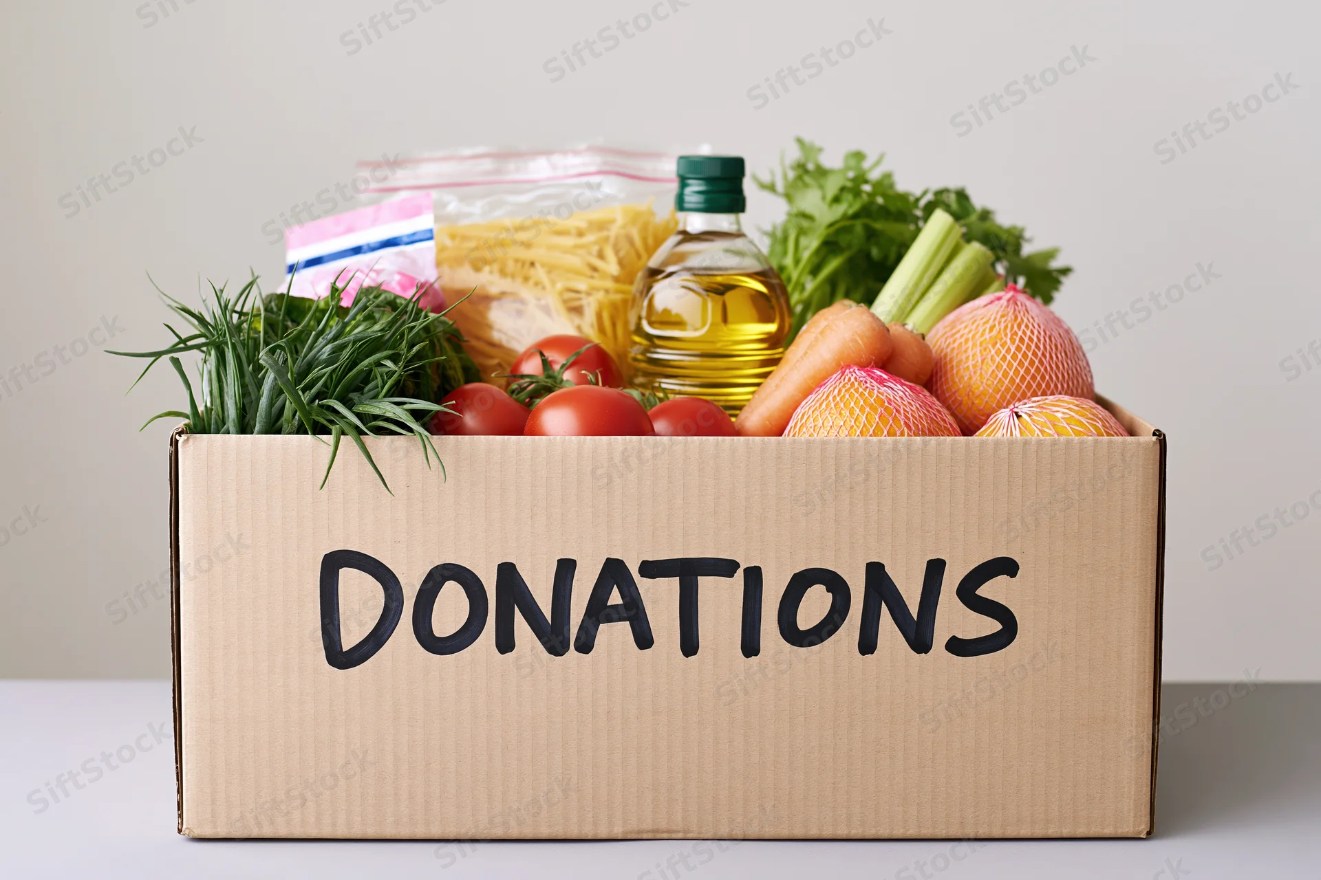 Cardboard box labeled donations filled with fresh vegetables, pasta, oil and other groceries on a table