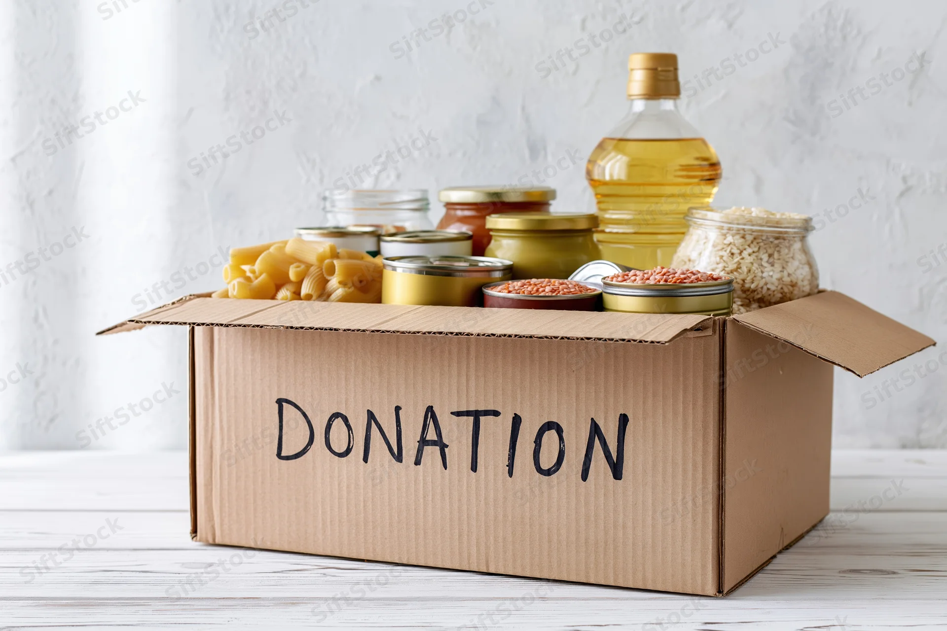 Cardboard donation box filled with nonperishable food items on a white wooden surface