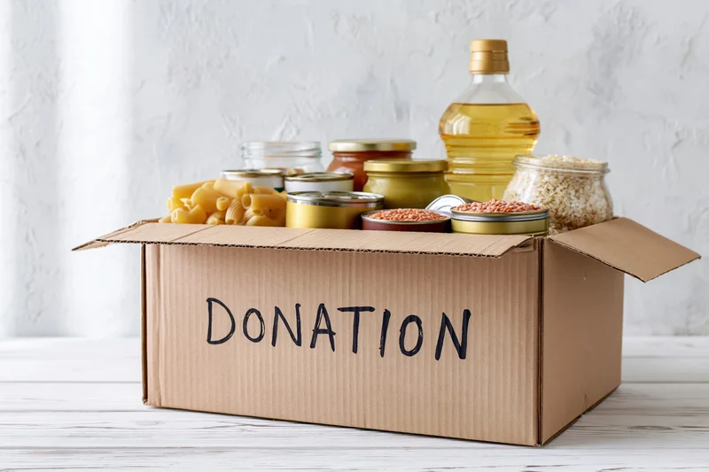 Cardboard donation box filled with nonperishable food items on a white wooden surface