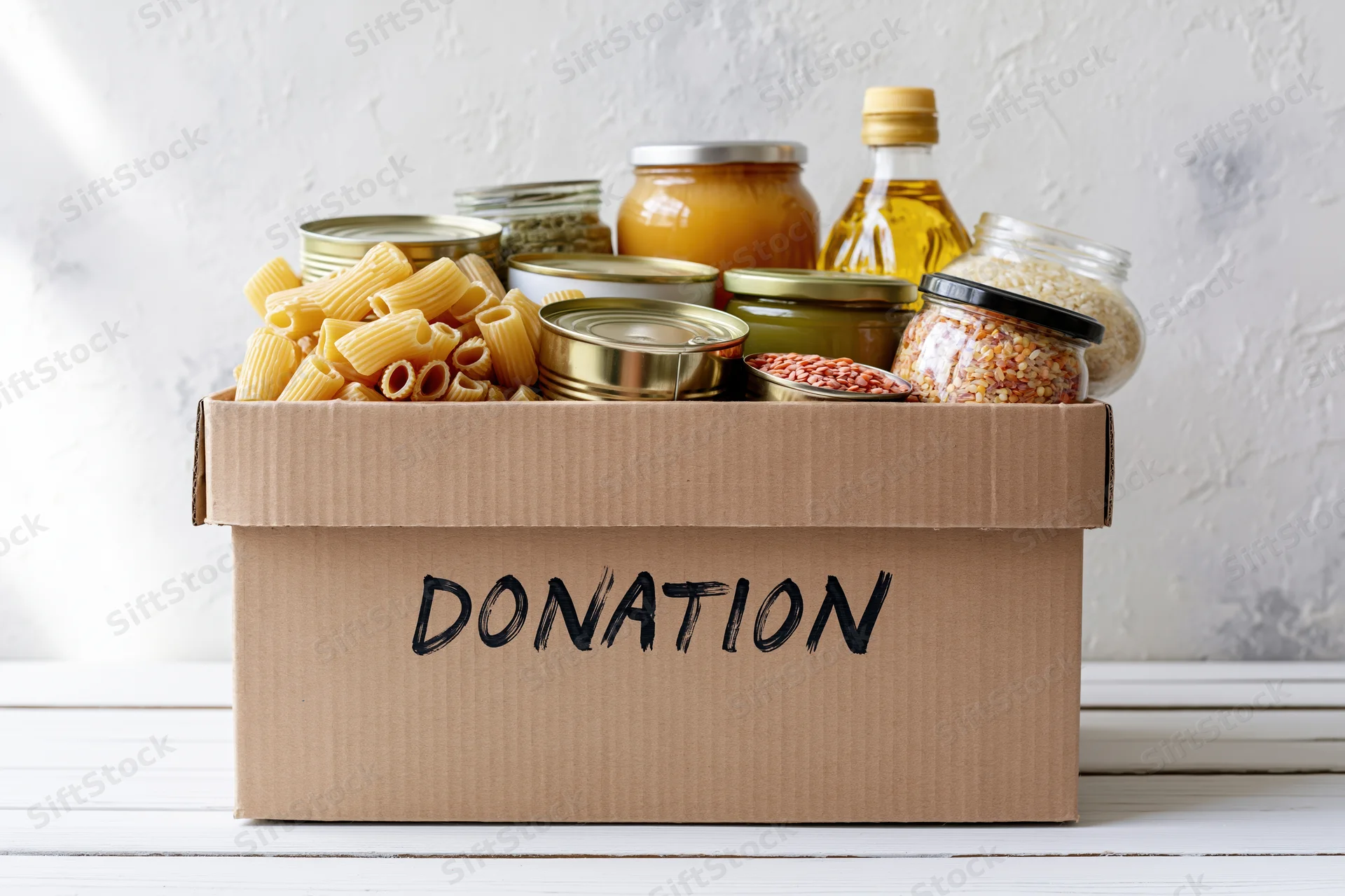 Cardboard box labeled donation filled with canned goods and pasta on white surface